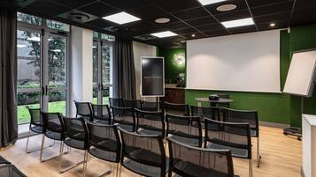 Une salle de conférence équipée d’un projecteur, d’un écran et d’un mur vert.