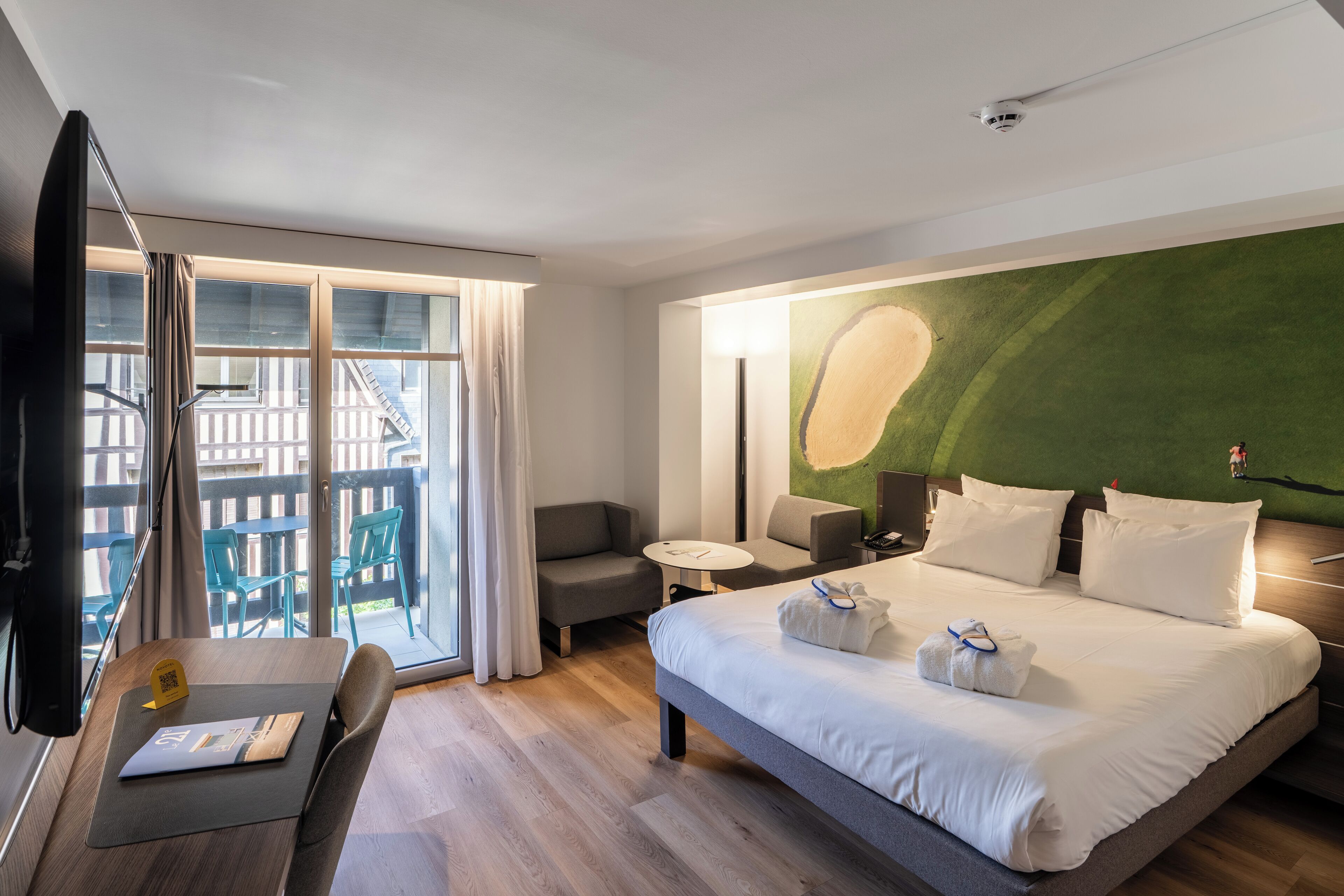 Habitación de hotel con cama, escritorio, silla, una mesita y balcón con sillas.