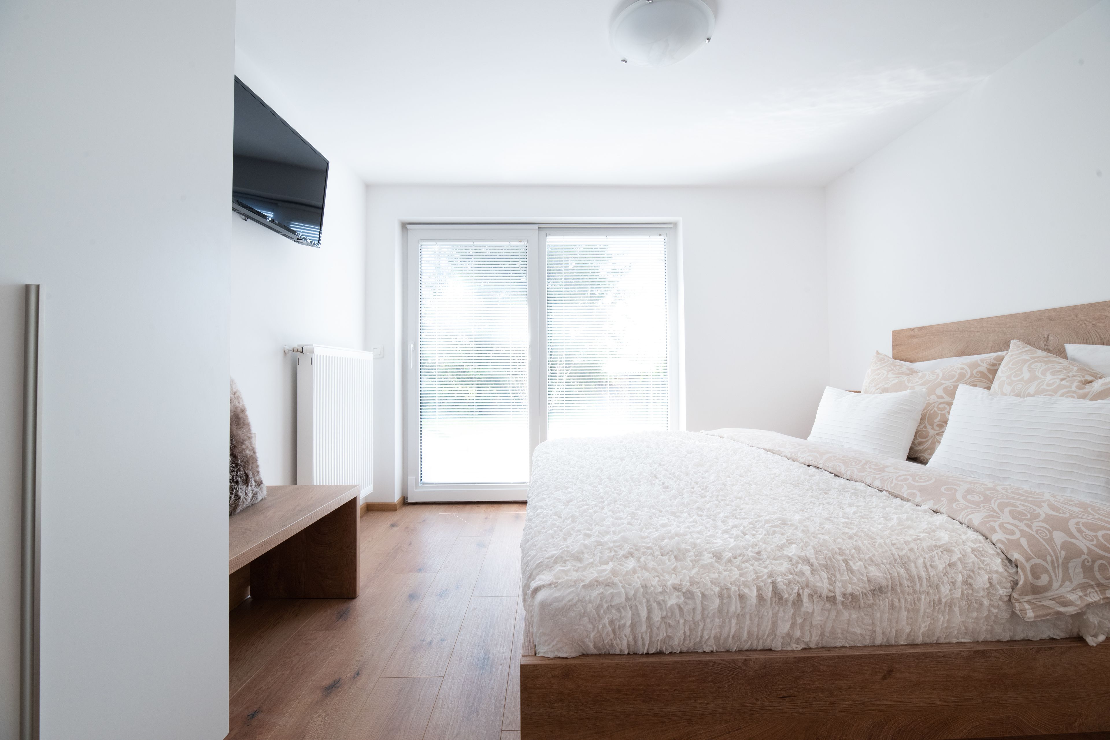 A bedroom with a large bed, a wooden headboard, a bench, and a sliding glass door leading to a balcony.