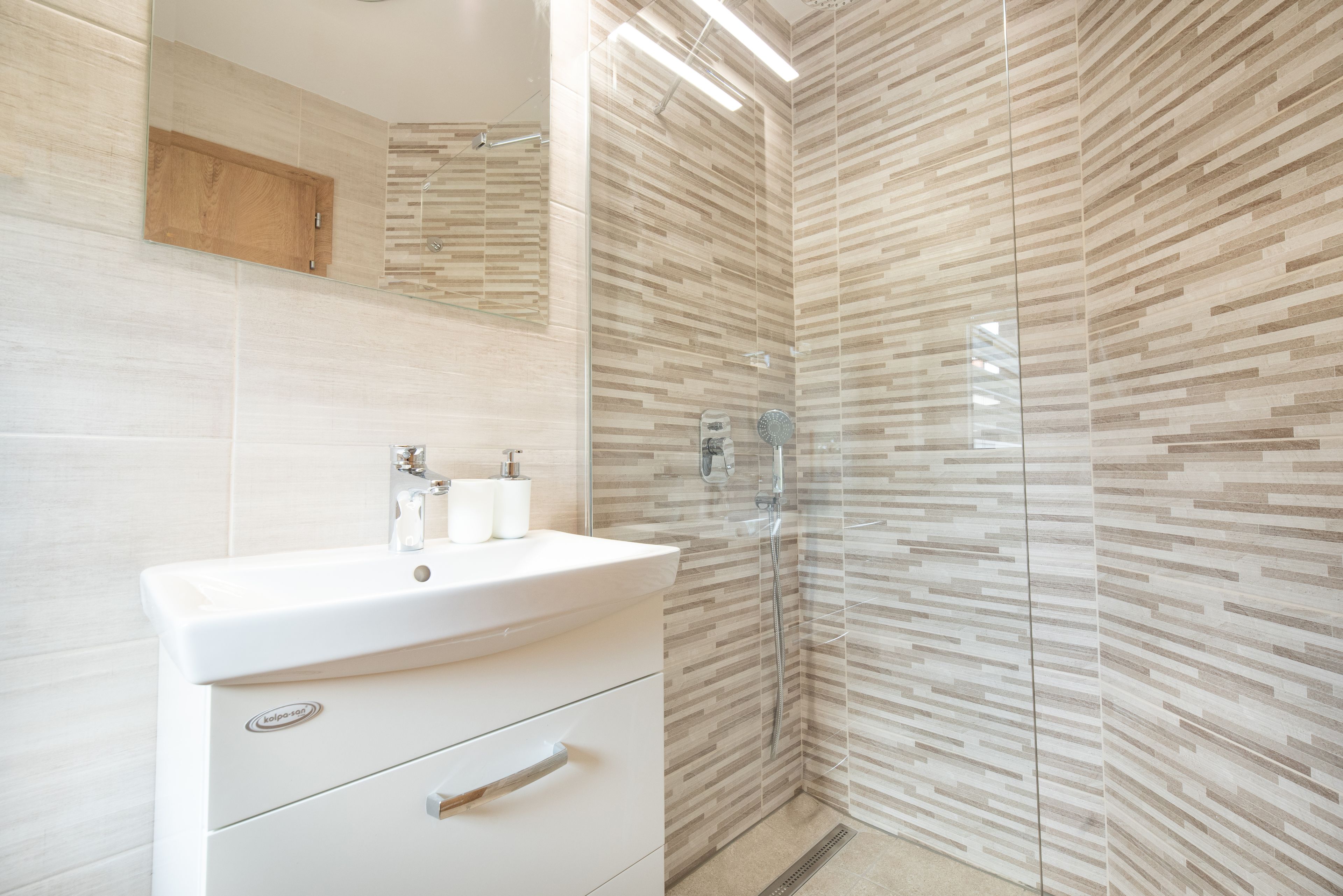 Un baño moderno con lavamanos blanco, espejo y cabina de ducha con paredes de vidrio.