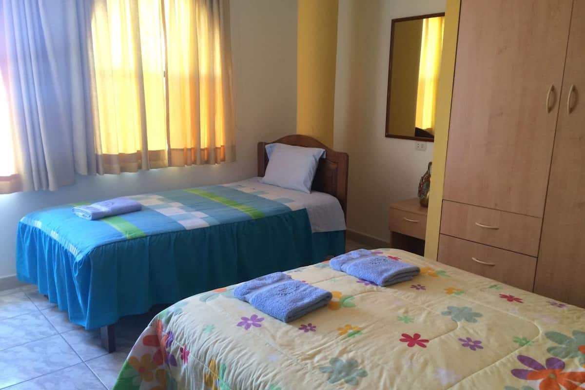 A bedroom with two beds, a nightstand, a wardrobe, and a window with curtains.