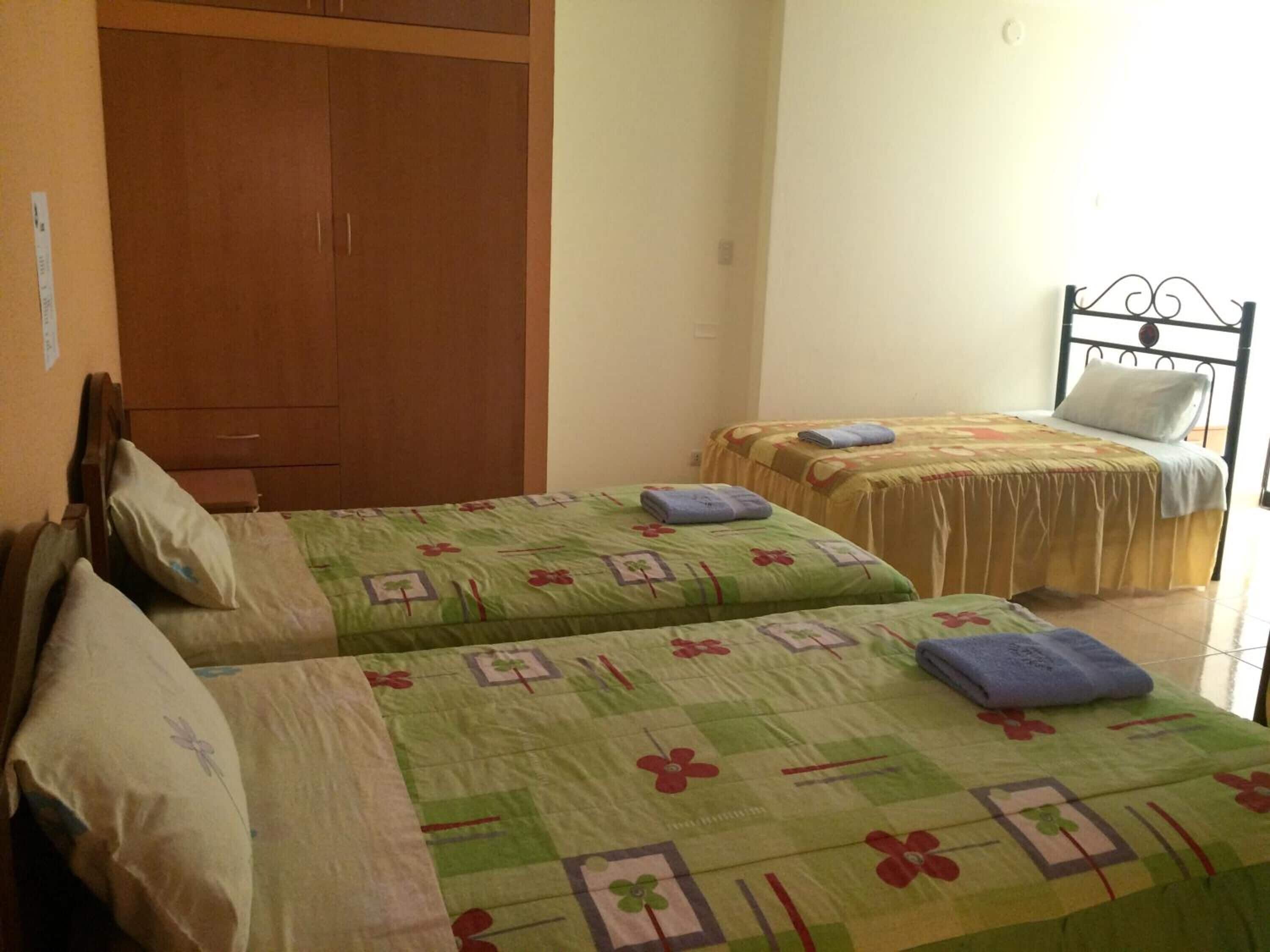 Una habitación con dos camas individuales, un armario de madera y una estructura metálica para la cama.