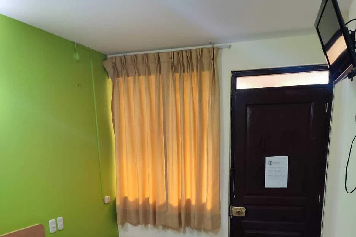 A hotel room with a bed, a nightstand, a small table, a window with curtains, and a door.