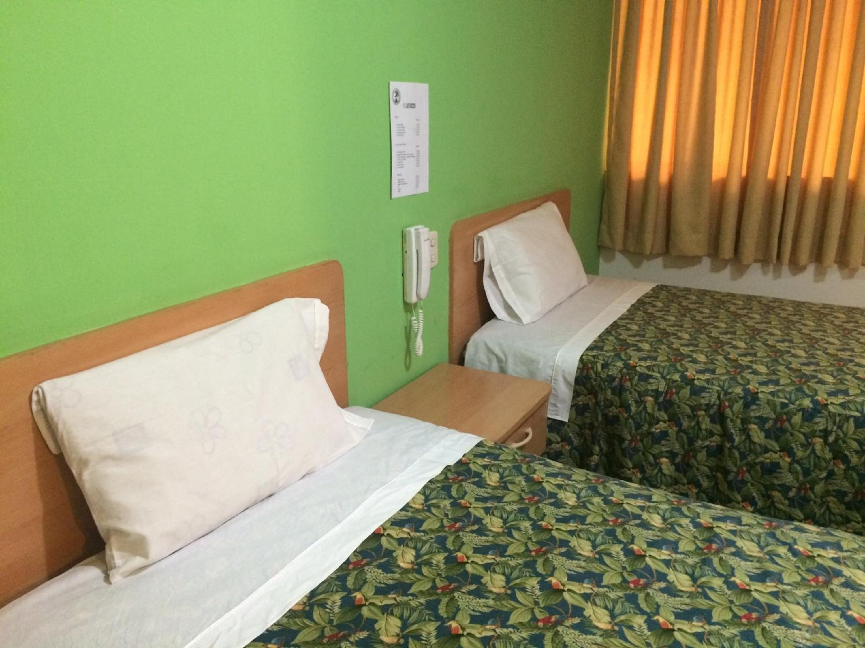 A hotel room with two beds, a bedside phone, and a green wall.