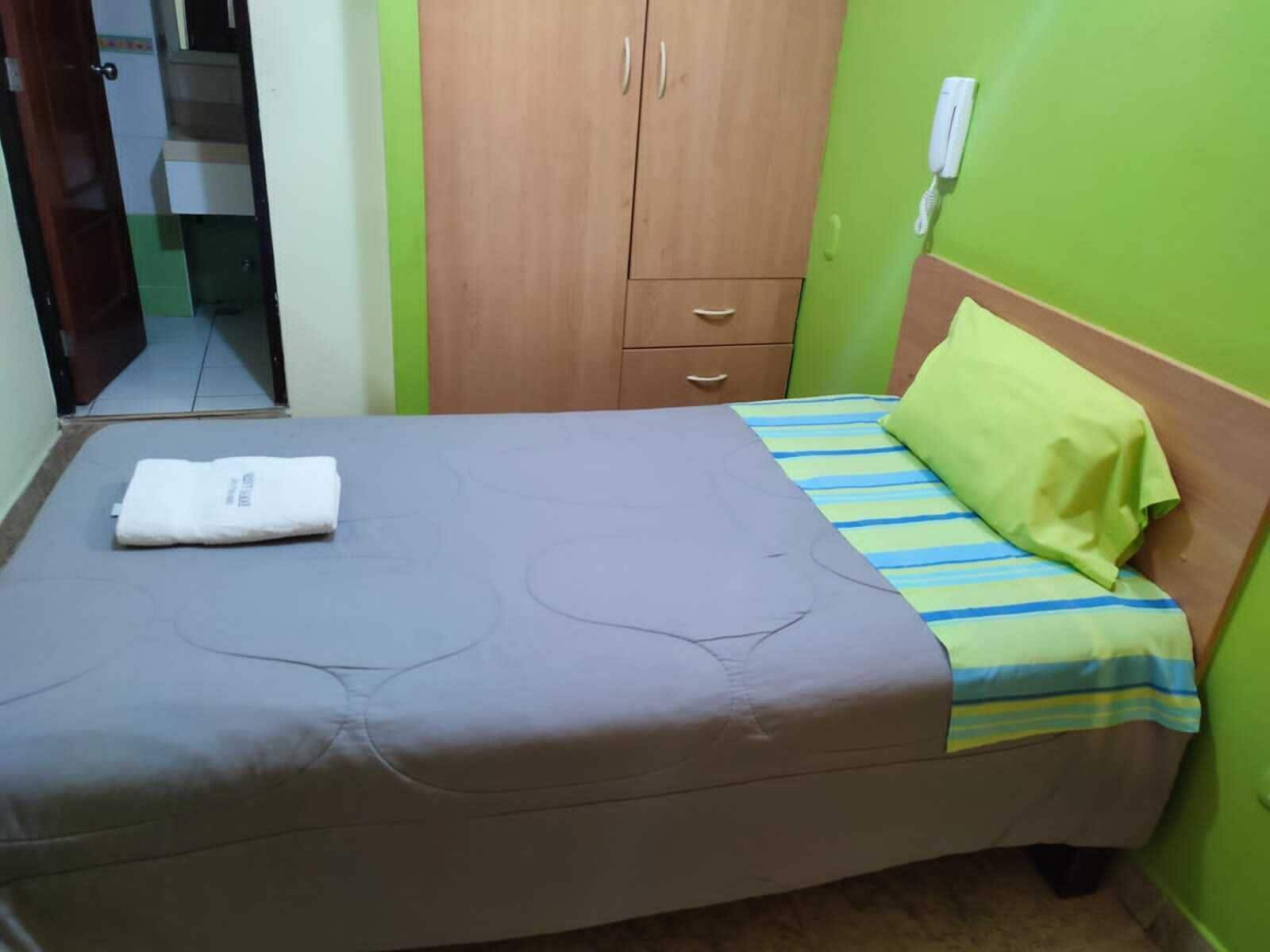 A single-bed room with a wooden wardrobe, a green wall, and a telephone.