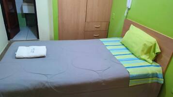 A single-bed room with a wooden wardrobe, a green wall, and a telephone.
