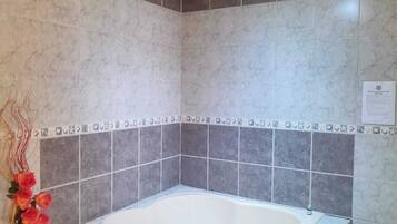A modern bathroom with a freestanding bathtub, tiled walls, and a decorative vase with flowers.