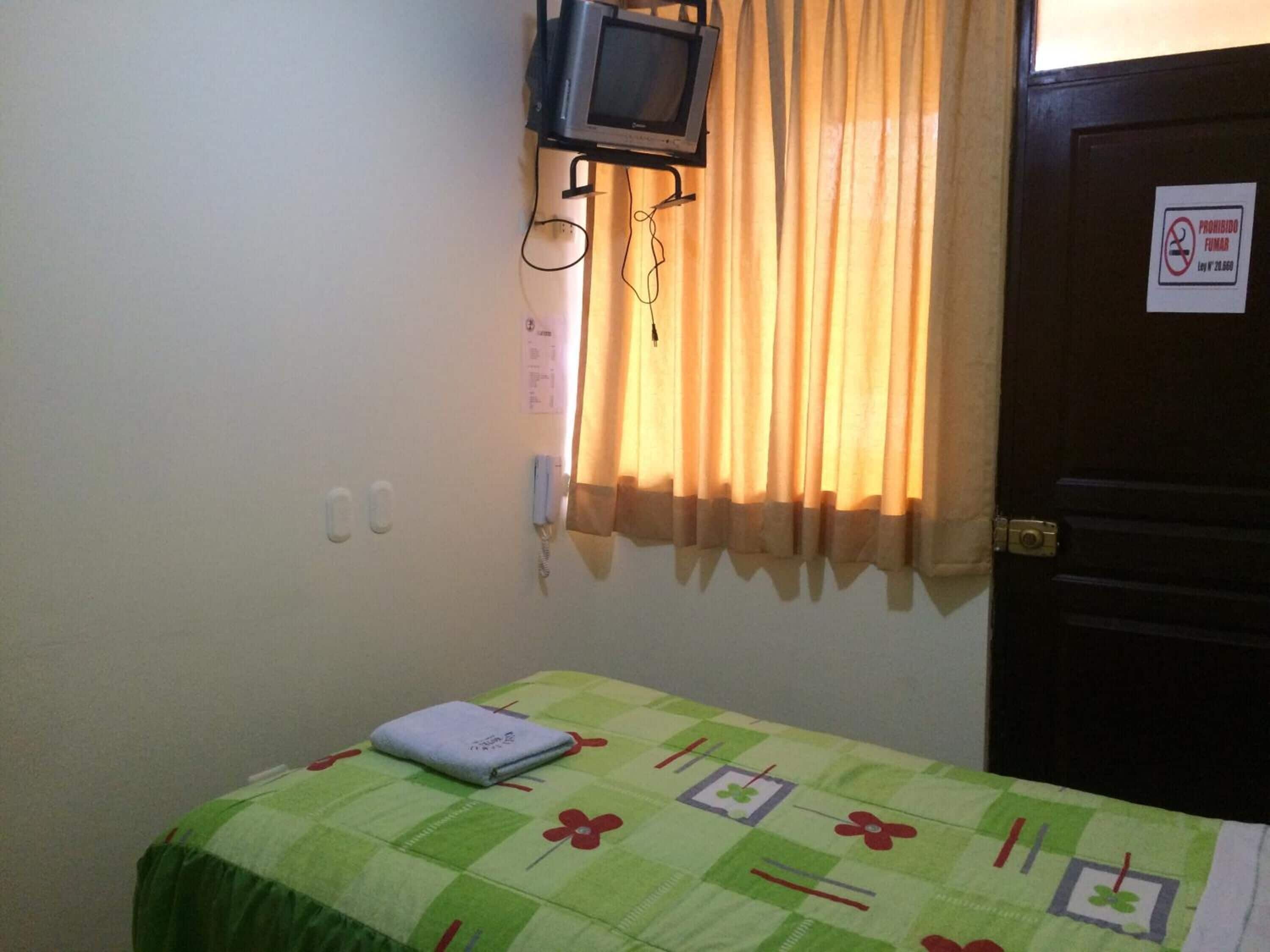 A small room with a bed, a television mounted on the wall, and a door with a sign.