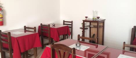 Un comedor con mesas cubiertas de manteles rojos, sillas de madera y un pequeño armario de madera con cristalería.