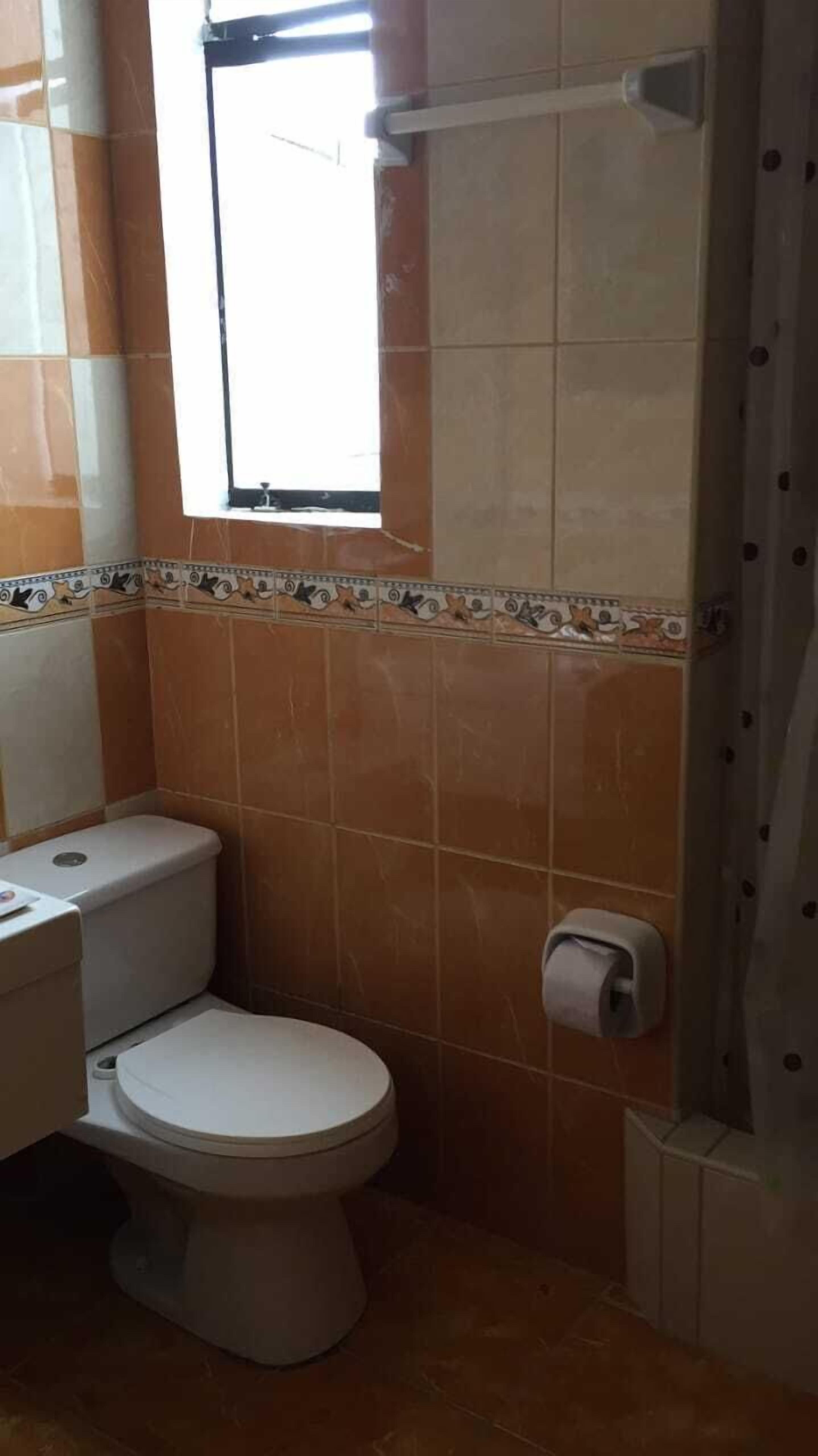 Un baño con inodoro, cortina de ducha y ventana.