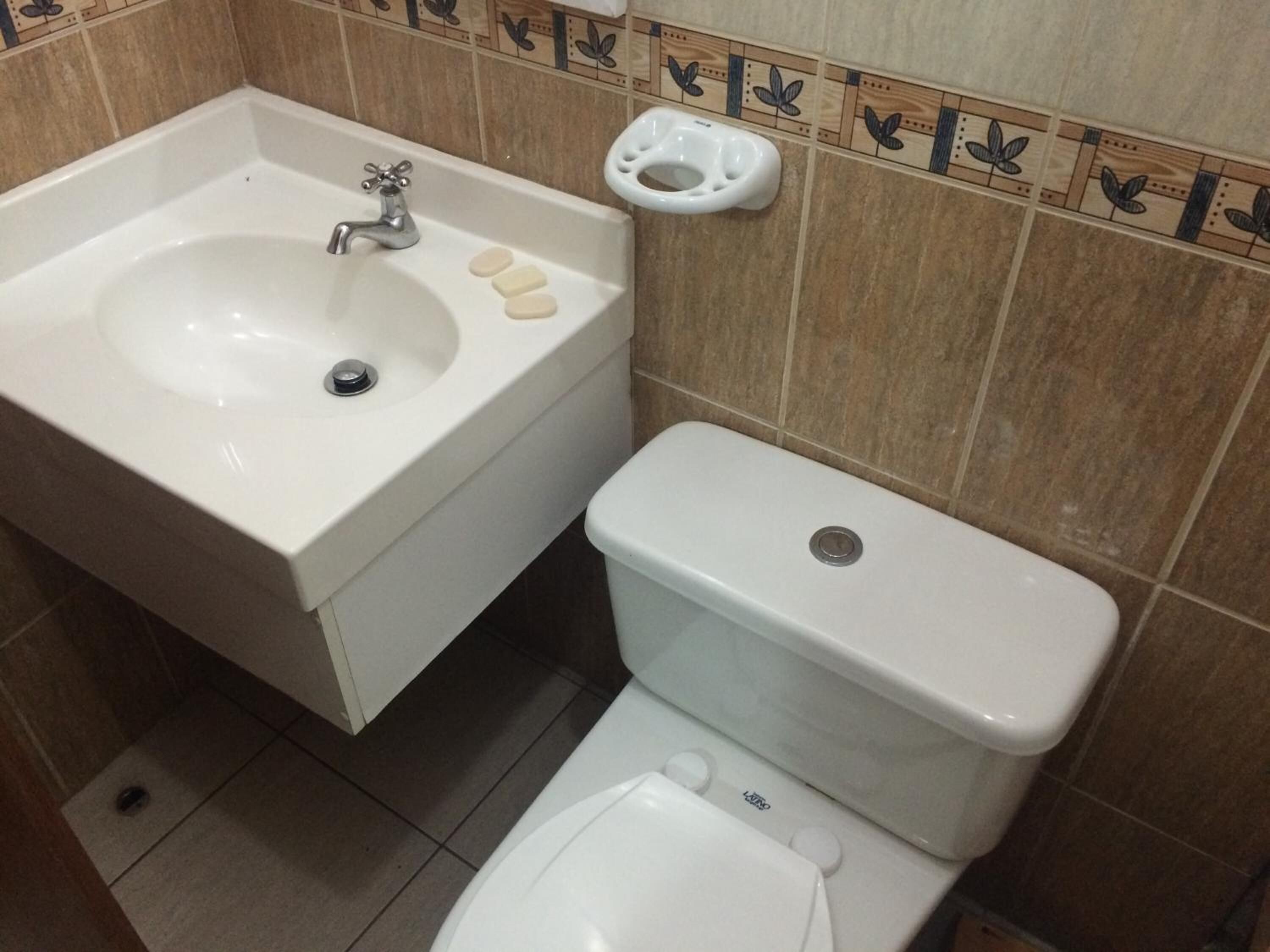 A bathroom with a sink, toilet, and a small shelf with soap.