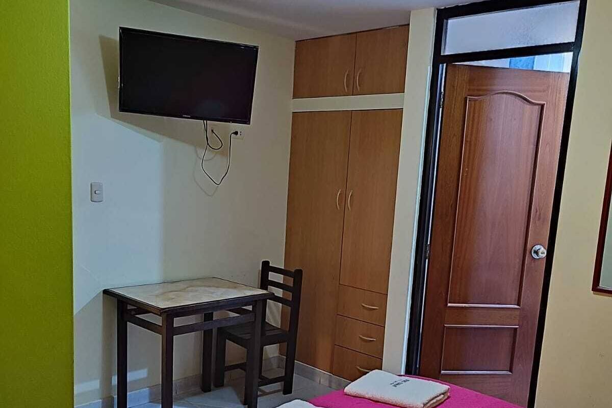 A bedroom with a bed, a desk, a chair, a television, and a wardrobe.