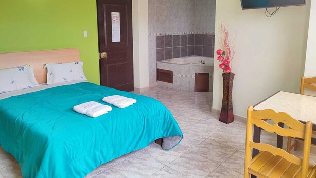 A hotel room with a bed, a desk, a chair, a TV, and a bathroom with a bathtub. - Hotel Misky Samay (Ayacucho)