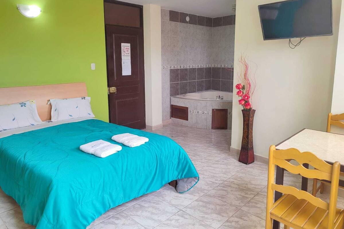 A hotel room with a bed, a desk, a chair, a TV, and a bathroom with a bathtub.