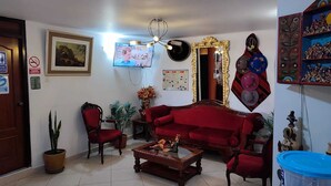 A living room with a red sofa, a wooden coffee table, a TV, a chandelier, and a wall with decorative items and a map. - Hotel Misky Samay (Ayacucho)