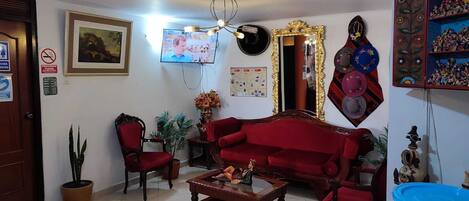 Uma sala de estar com um sofá vermelho, uma mesa de centro de madeira, uma televisão, um candelabro e uma parede decorada com objetos e um mapa.