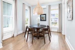 Uma sala de jantar com uma mesa de madeira redonda, quatro cadeiras, um lustre e um quadro na parede.