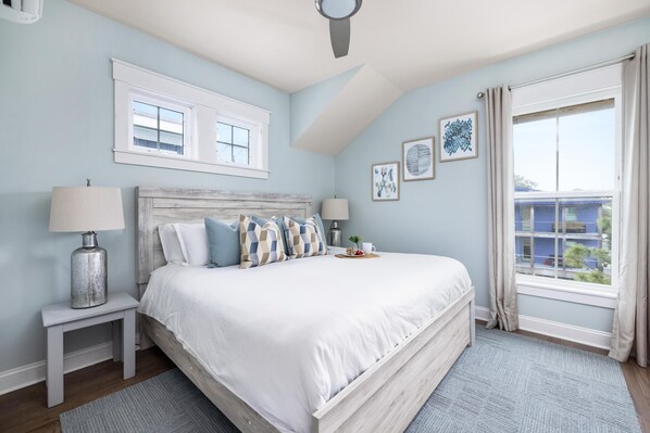 Une chambre à coucher avec un grand lit, deux tables de chevet, un ventilateur de plafond et une fenêtre avec des rideaux.
