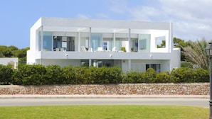 Een modern huis met twee verdiepingen, grote glasramen, een stenen muur ervoor en een verzorgd gazon.