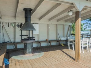 Un espace extérieur abrité, équipé d’un poêle à bois, de bancs et d’une table avec des chaises.