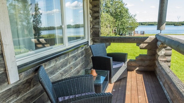 Een houten terras met rieten meubilair en een glazen raam met uitzicht op een meer.