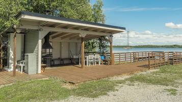 A covered outdoor area with a grill, seating, and a view of a lake.