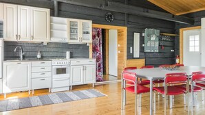 Een moderne keuken met witte kasten, een fornuis en een spoelbak. Er is een eethoek met een tafel en rode stoelen.