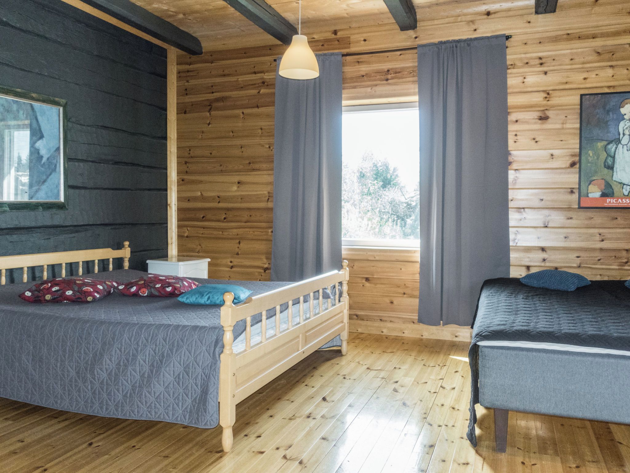 Een kamer met een houten vloer, een bed met hoofdeinde, een nachtkastje, een hanglamp en een raam met gordijnen.