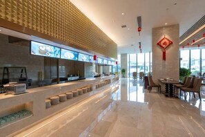 A modern restaurant with a long counter, multiple seating areas, and a decorative wall. - Jingcheng International Hotel (Yangzhou)
