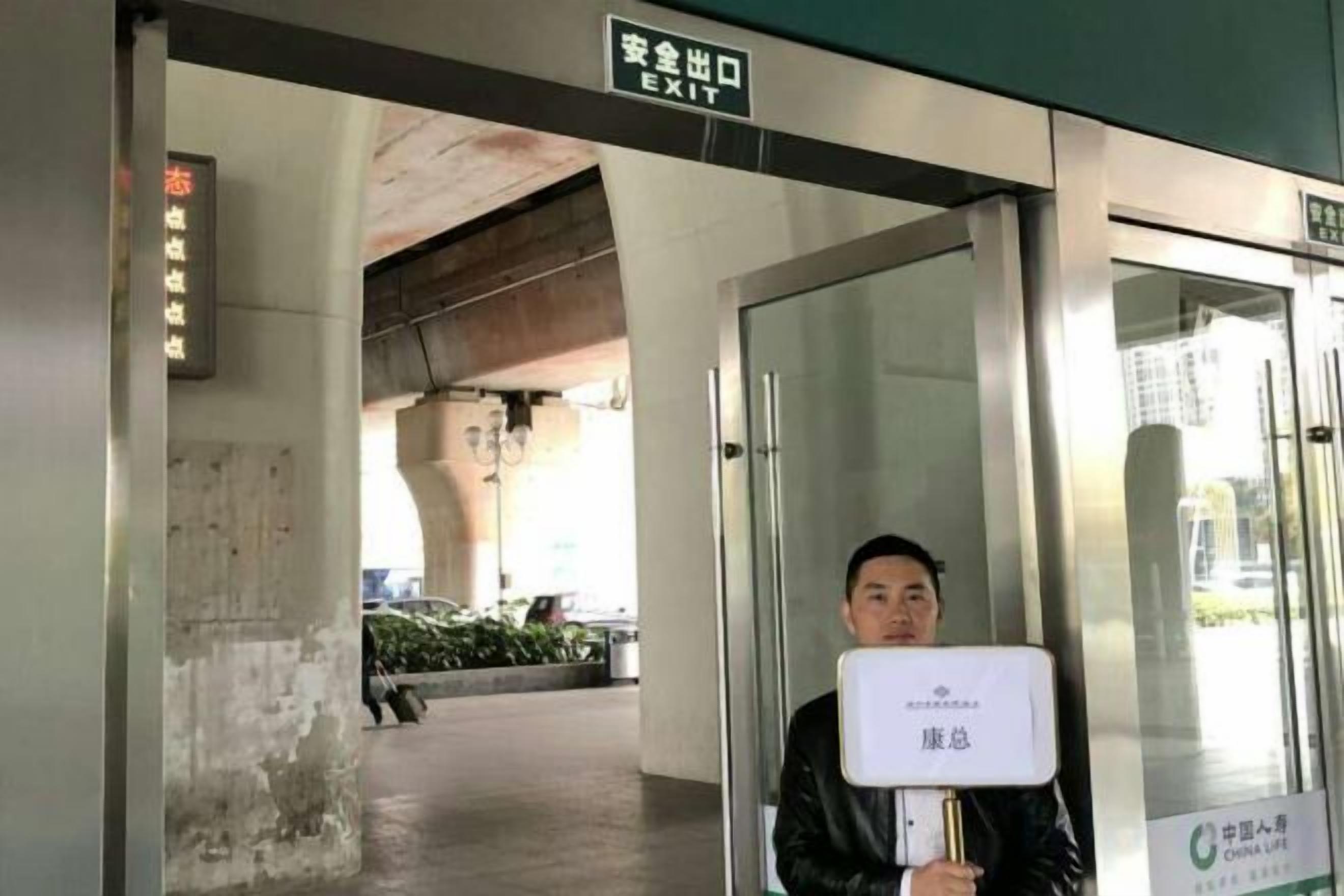 Un hombre sostiene un cartel en una puerta de salida, con un letrero superior que indica 'EXIT'.