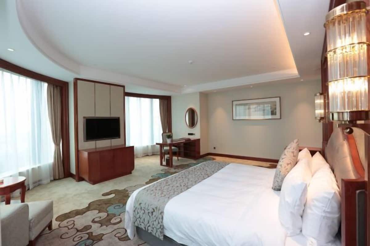 Una habitación de hotel con una cama grande, televisión, escritorio y una silla.