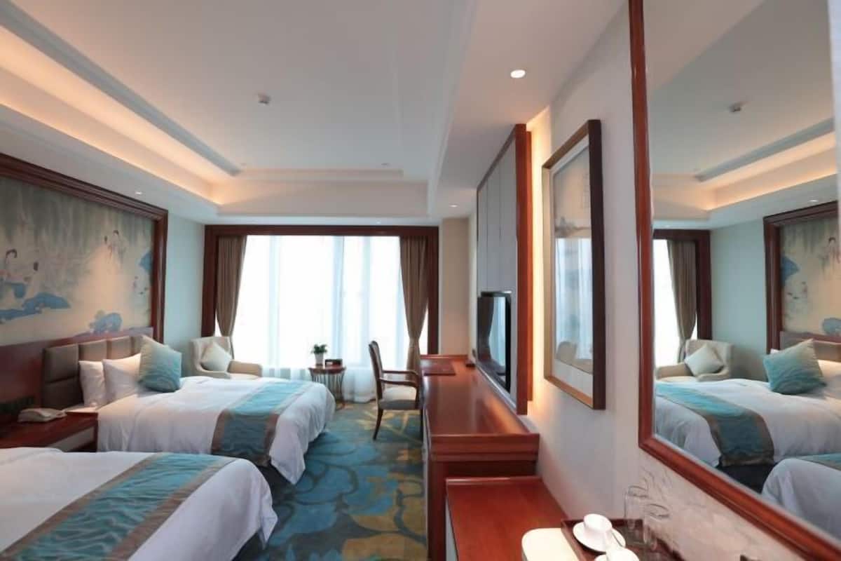Habitación de hotel con dos camas, televisión, escritorio y un espejo grande.