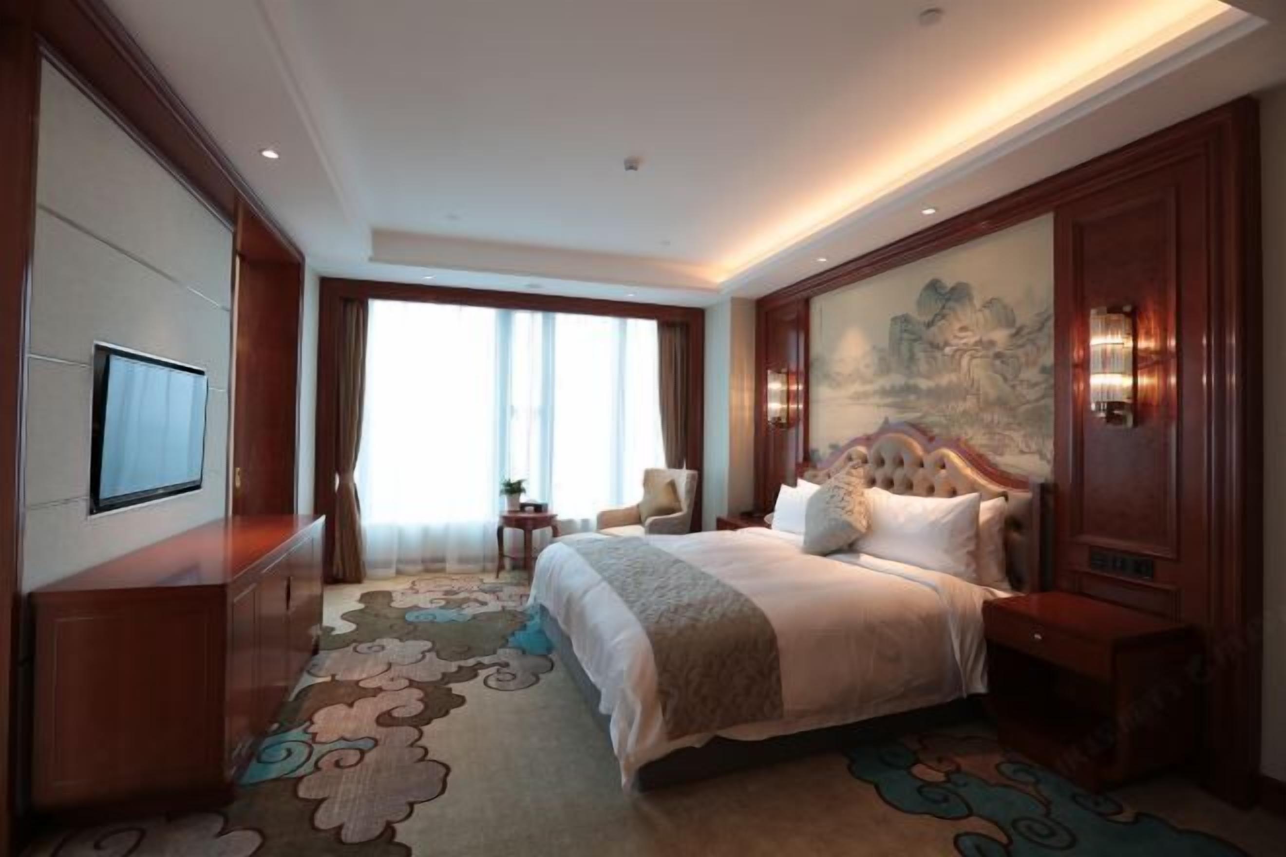 A spacious hotel room with a large bed, a television, a desk, and a painting on the wall.