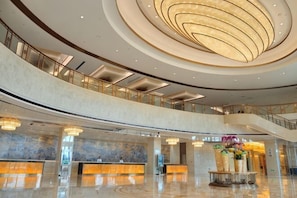 A spacious lobby with a marble reception desk, a central decorative fountain, and a modern ceiling design.