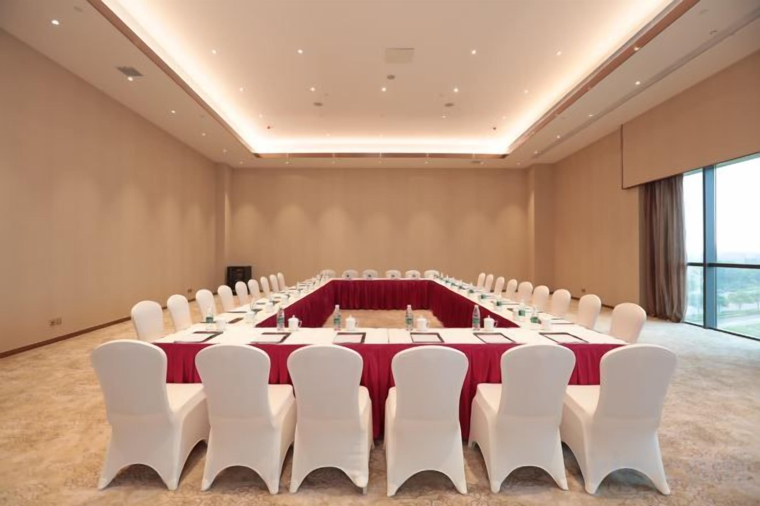 A conference room with a long table, white chairs, and a red tablecloth.
