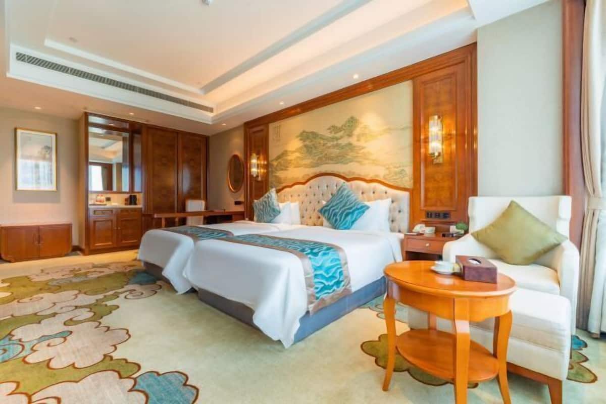 Habitación de hotel con una cama grande, una zona de estar con una silla, una mesita y un cuadro en la pared.