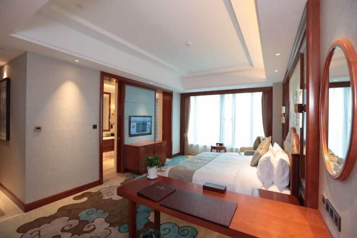 Una habitación de hotel con una cama grande, un escritorio con silla, un televisor y un espejo.