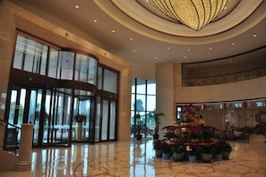 A spacious lobby with a revolving door, a large potted plant arrangement, and a high ceiling with a circular light fixture. - Jingcheng International Hotel (Yangzhou)
