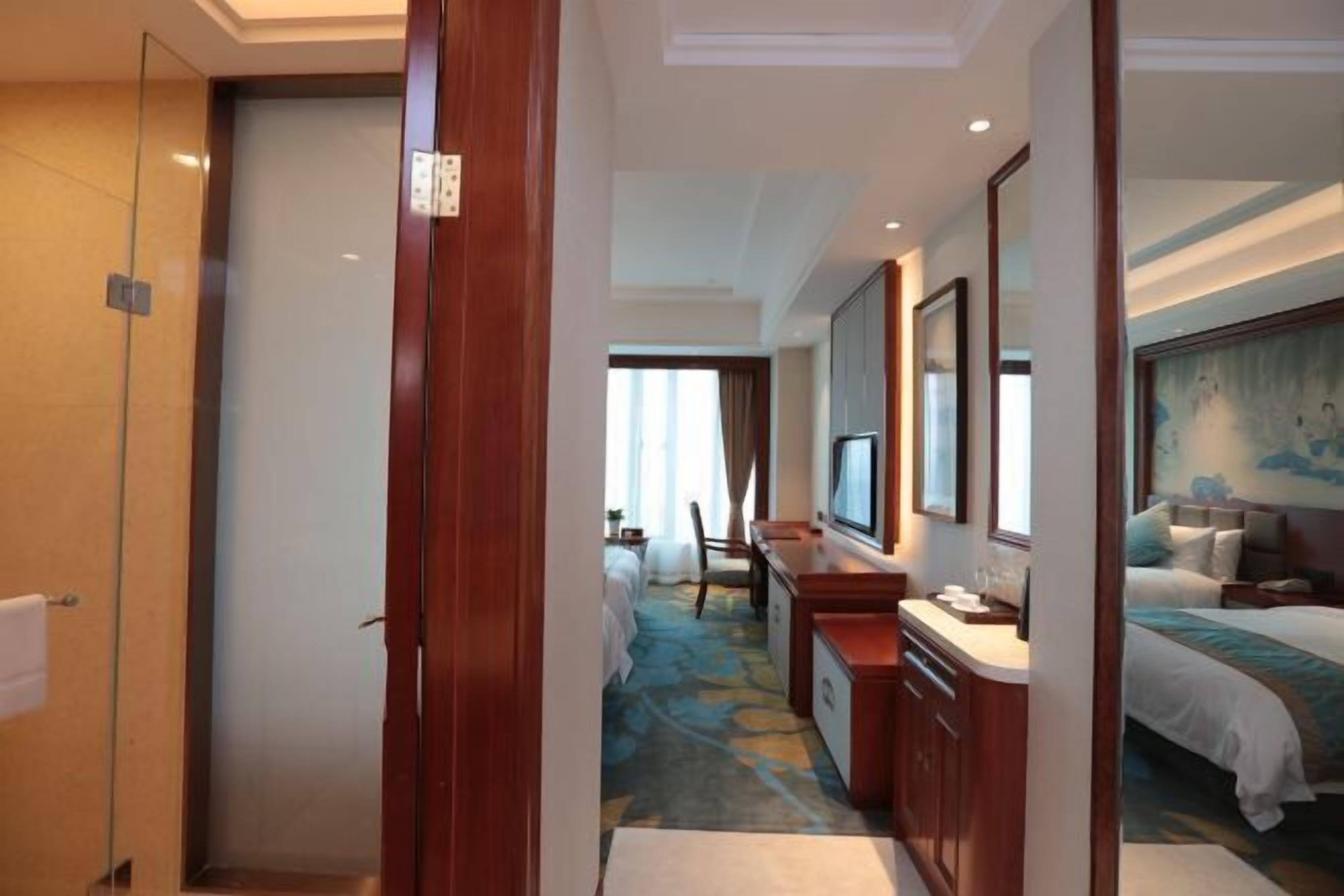 Habitación de hotel con cama, escritorio, silla, televisión y baño con cabina de ducha de vidrio.