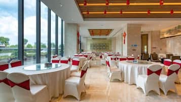A banquet hall with round tables and chairs, large windows, and a modern interior design.