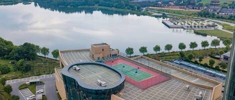 A modern building with a curved glass facade, a rooftop sports area, and a view of a lake and distant buildings.