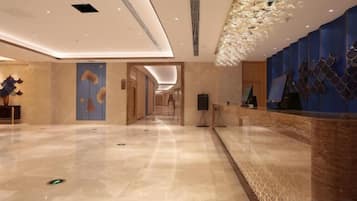 A hotel lobby with a reception desk, a large decorative ceiling, and a marble floor.