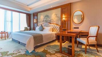 A hotel room with a large bed, a desk, a chair, a round mirror, and a painting on the wall.