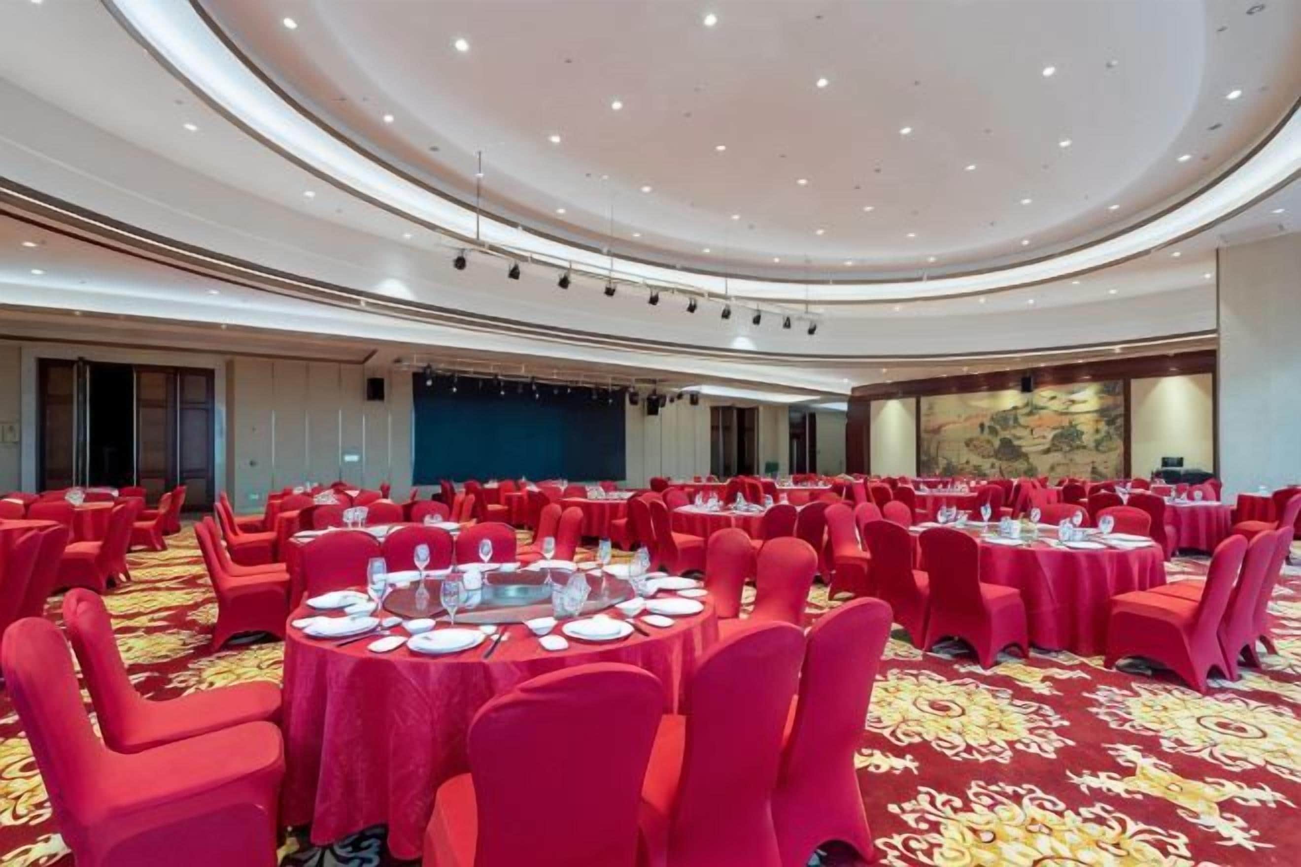 Un salón de conferencias amplio con mesas redondas, sillas rojas y piso alfombrado.