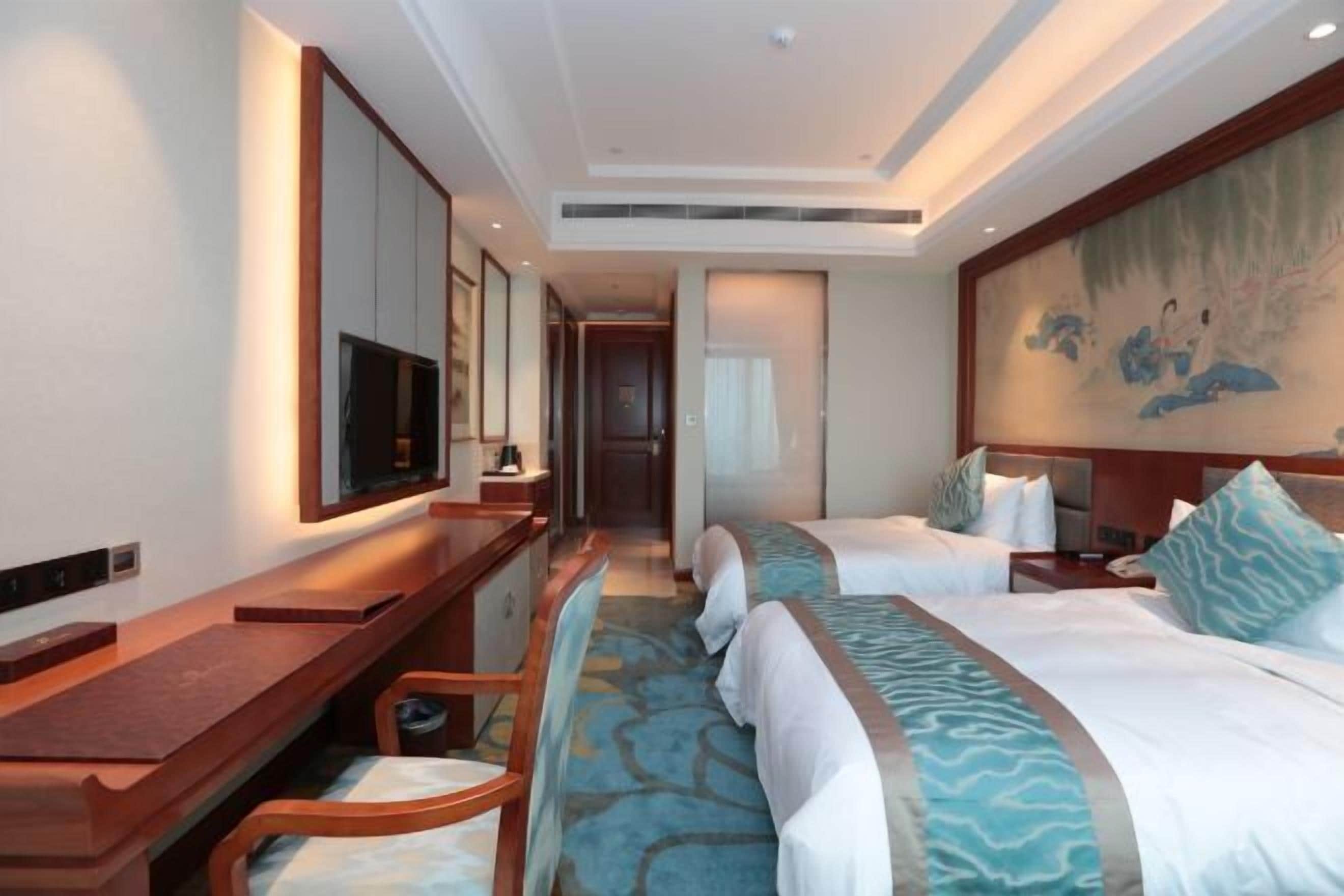 A hotel room with a bed, a desk, a chair, a television, and a painting on the wall.