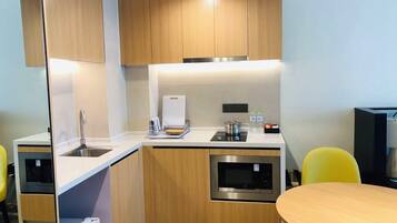 Cocina compacta con gabinetes de madera, un lavamanos de acero inoxidable, un microondas y una pequeña zona de encimera.