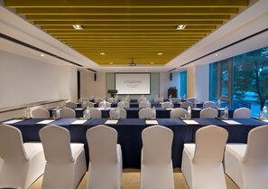 A conference room with a large screen, white chairs, and tables set for a meeting.