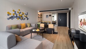 A modern living room with a sofa, coffee table, and TV. There is a dining area in the background.