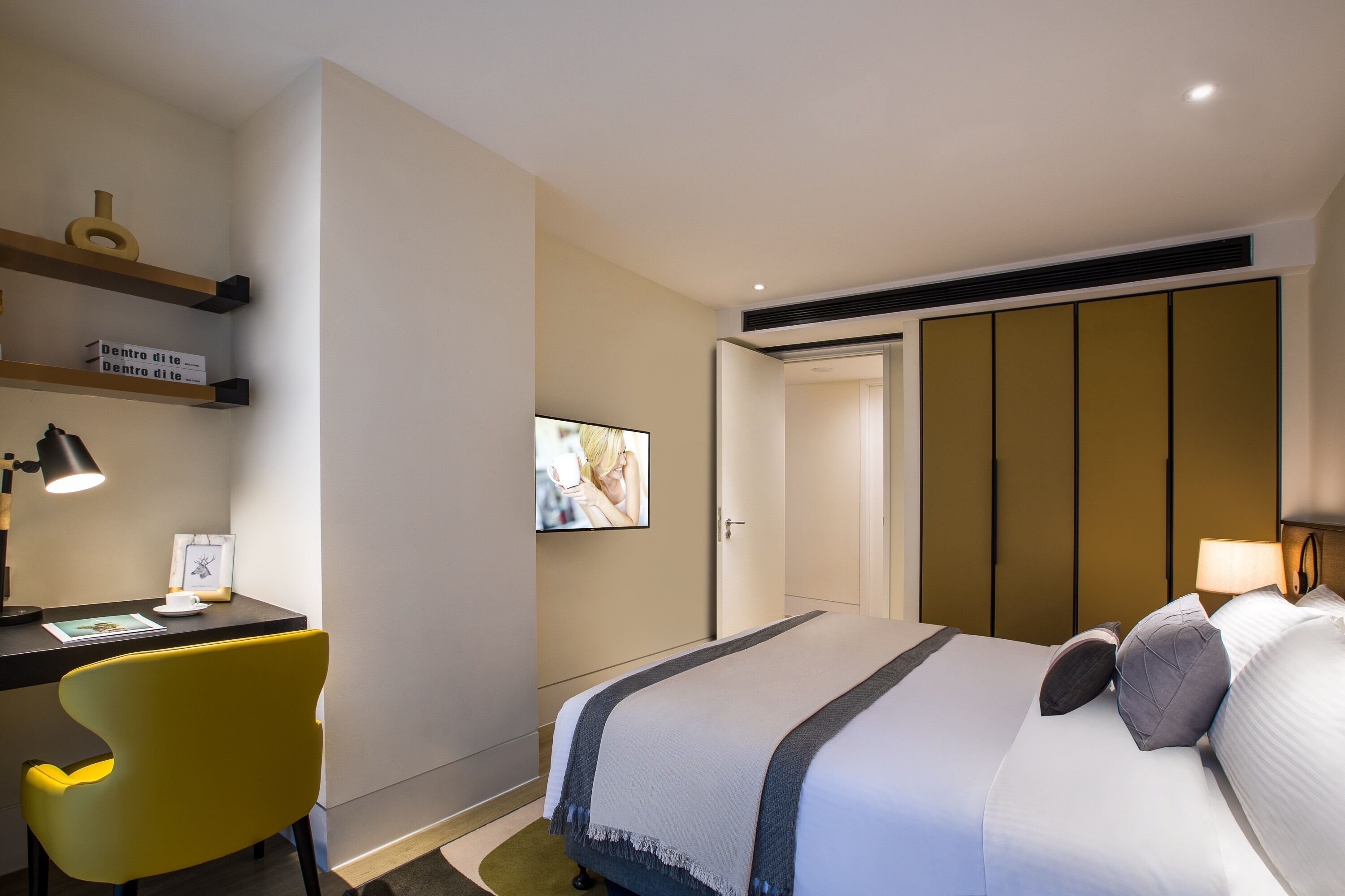 A hotel room with a bed, a desk with a chair, a television, and a wardrobe.