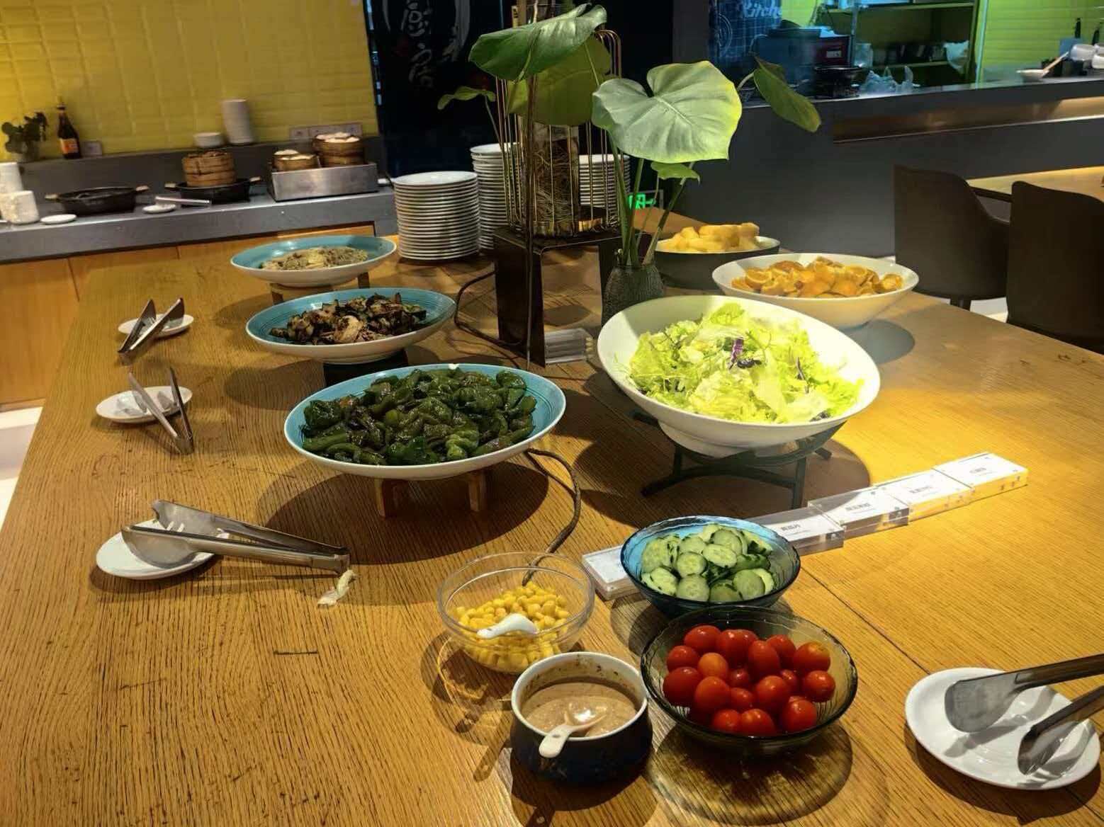 Un tavolo da buffet con diversi piatti, tra cui insalate, verdure e una ciotola di mais.